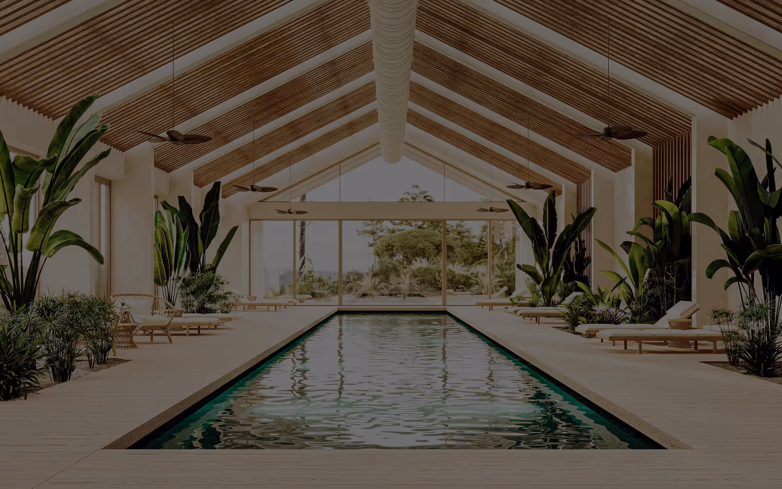 A long pool under a timber gable roof, flanked by planting and loungers, opening to the garden through the glazed gable.