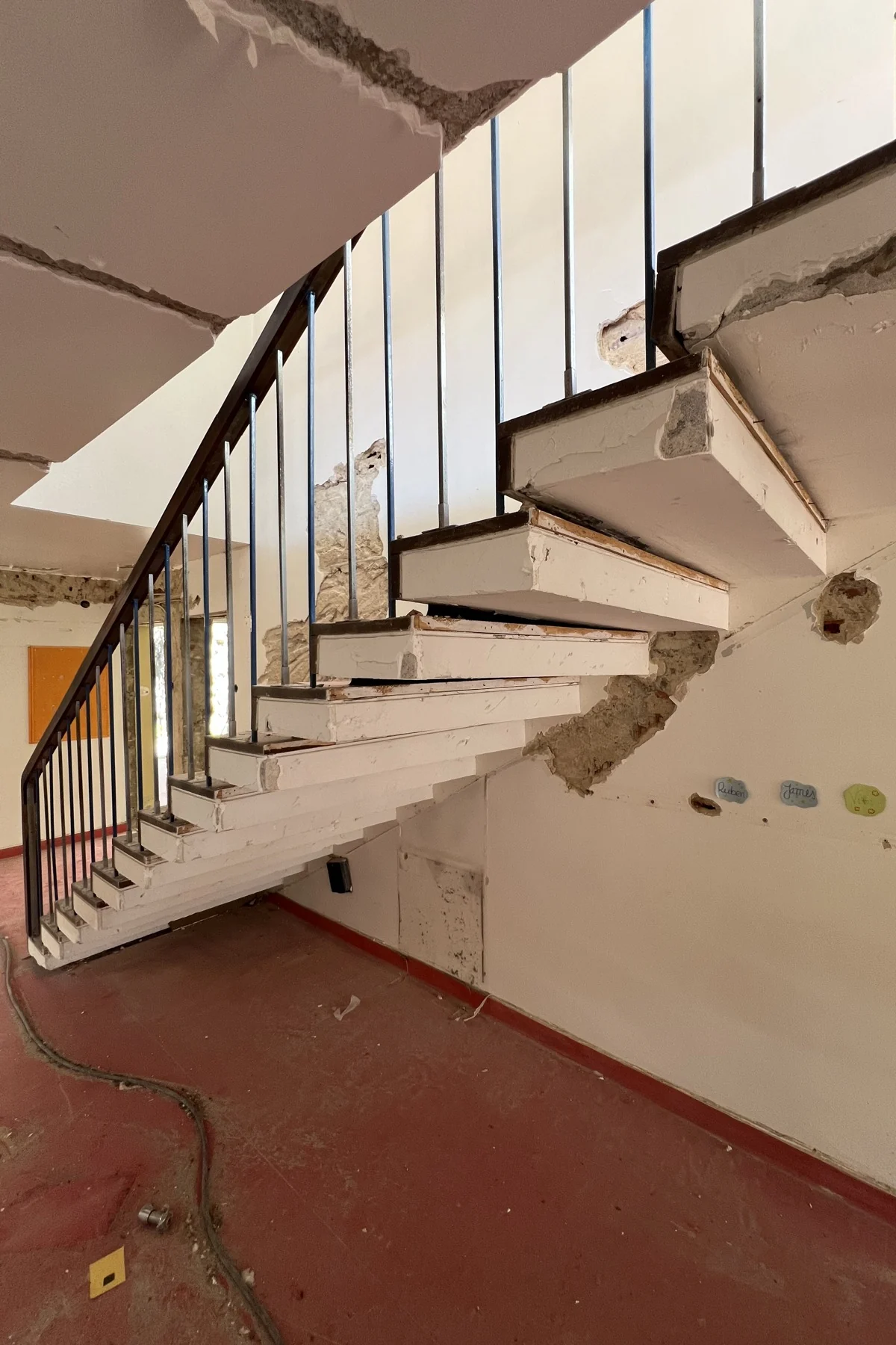The cantilevered stair: white treads out of the wall with no stringer beneath them, a balustrade of thin dark uprights, and the finish opened along the wall.