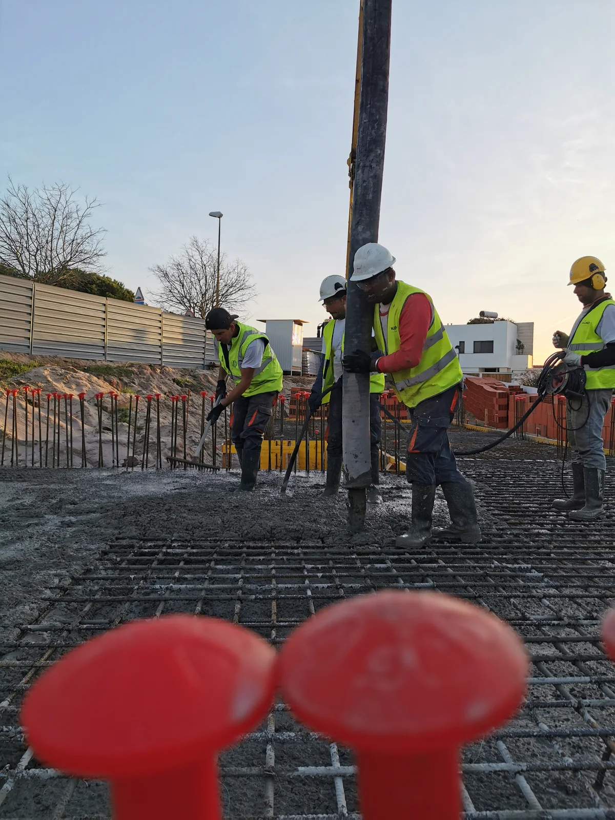A concrete pour at dusk, with a pump arm overhead and four workers in high-visibility clothing on the deck.