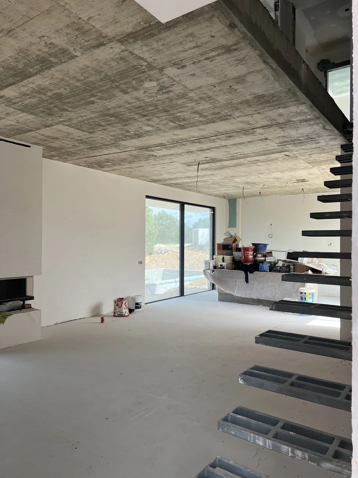 An interior with a steel and timber open stair installed, exposed concrete ceiling and full-height glazing onto the landscape.
