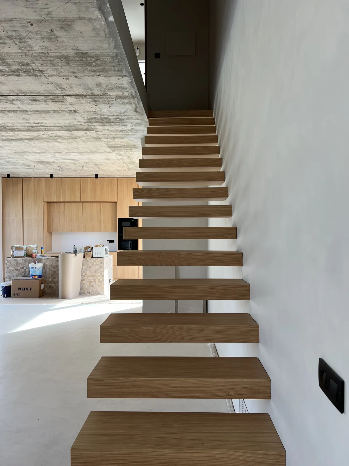 The finished stair: timber treads on steel stringers, open, against a white wall.