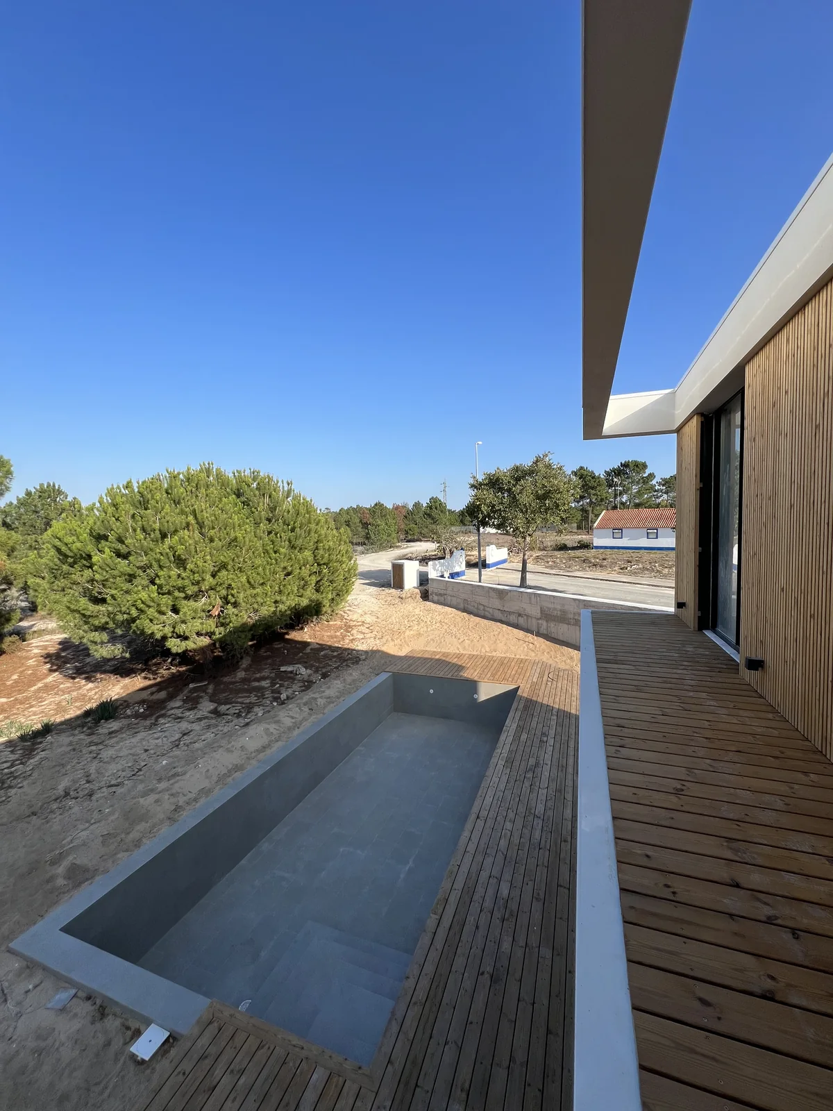 A pool with a timber deck along one side, low pines and open sky beyond.