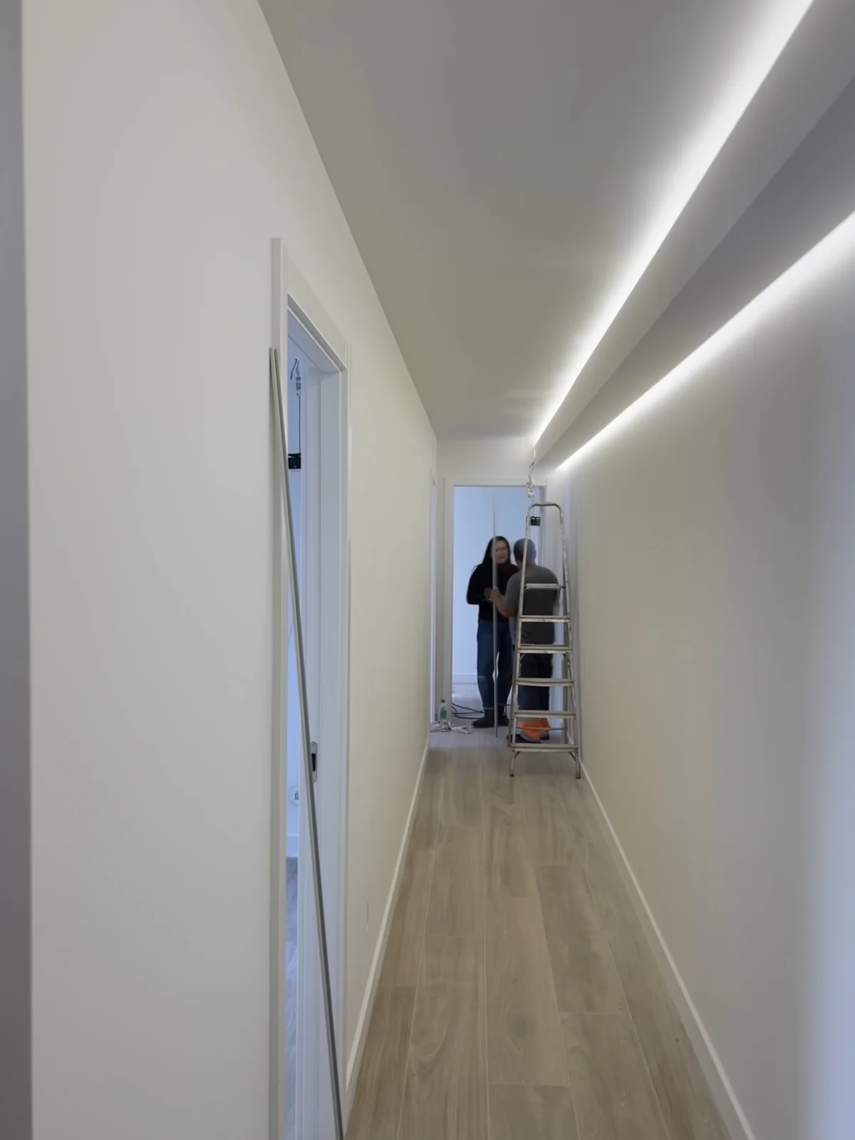 A narrow corridor with oak flooring, lit by a single continuous line of light recessed in the ceiling.