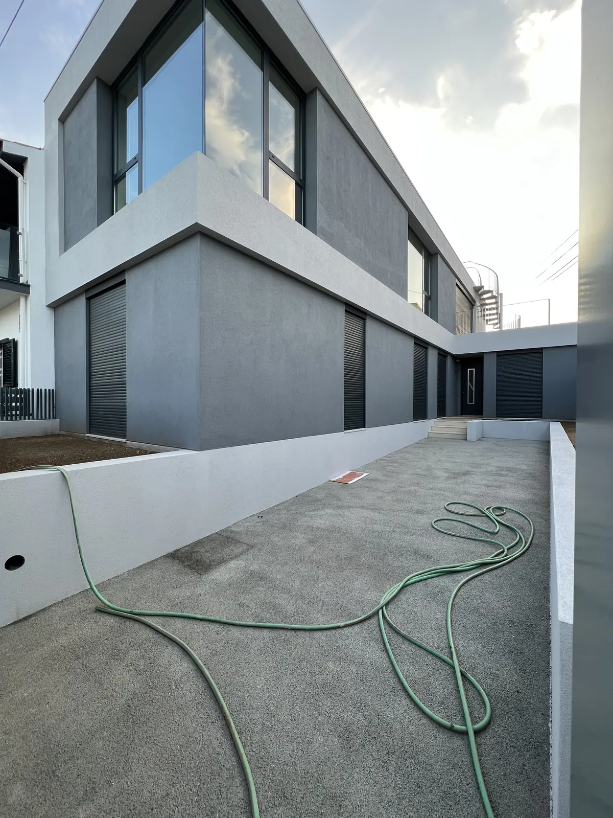 The finished façade in grey render and white, with a raised terrace and a garden hose across it.