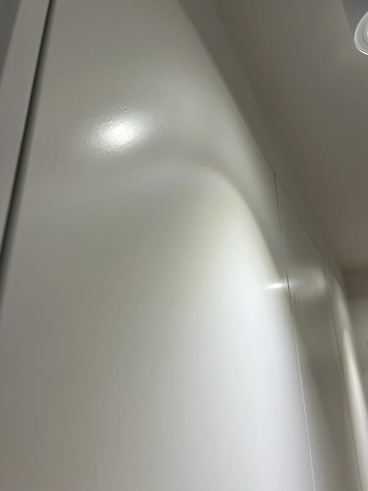 A white ceiling curving without a break into the wall below it, with a single recessed downlight.