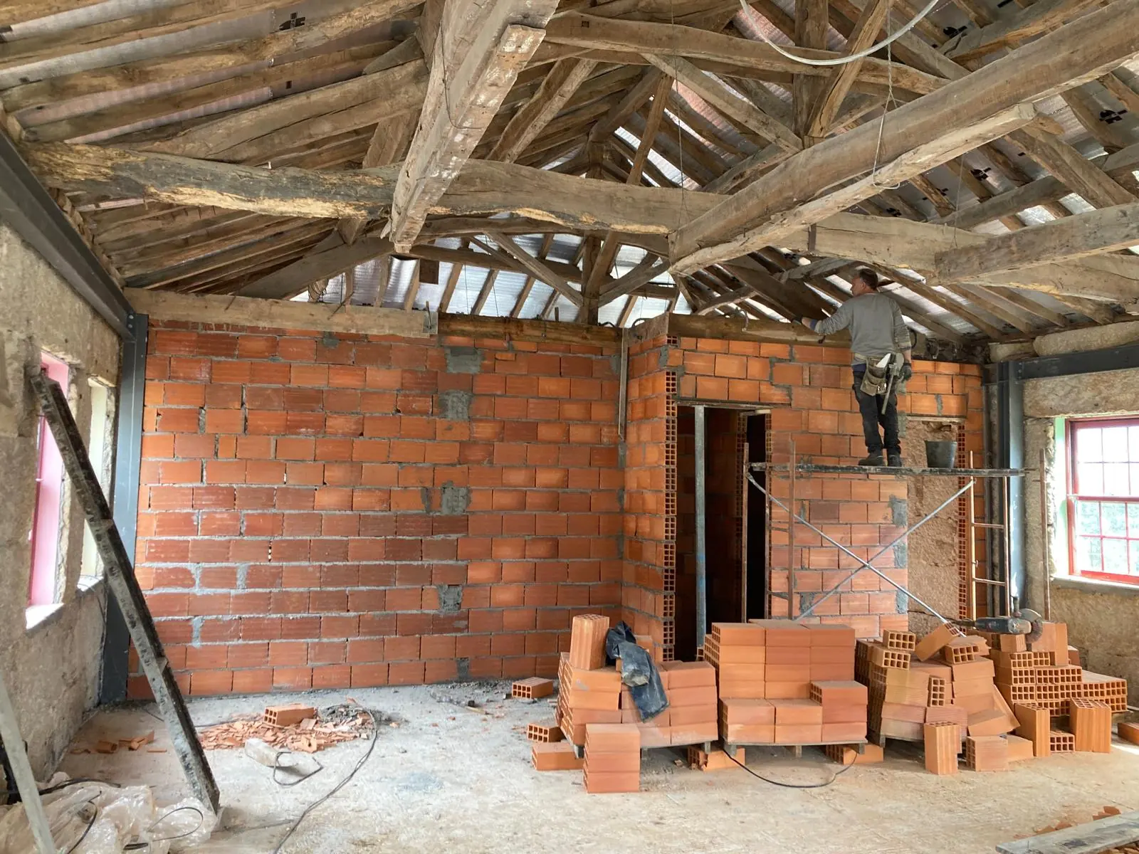Brick partitions going up inside the stone shell under the original roof structure, pallets of block on the floor and a worker on a ladder.