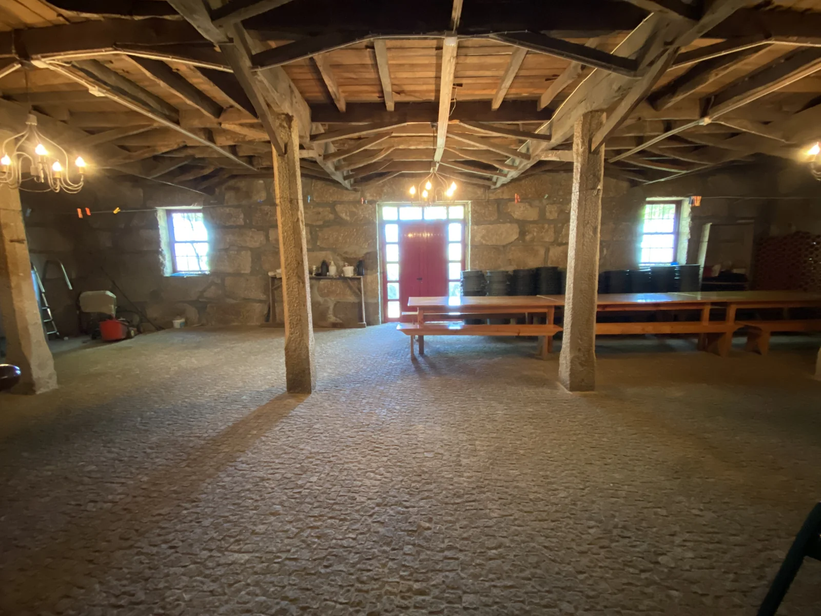 A large room in the farm building as found: granite walls, a floor of beaten earth, and a roof carried on rough timber posts and beams.