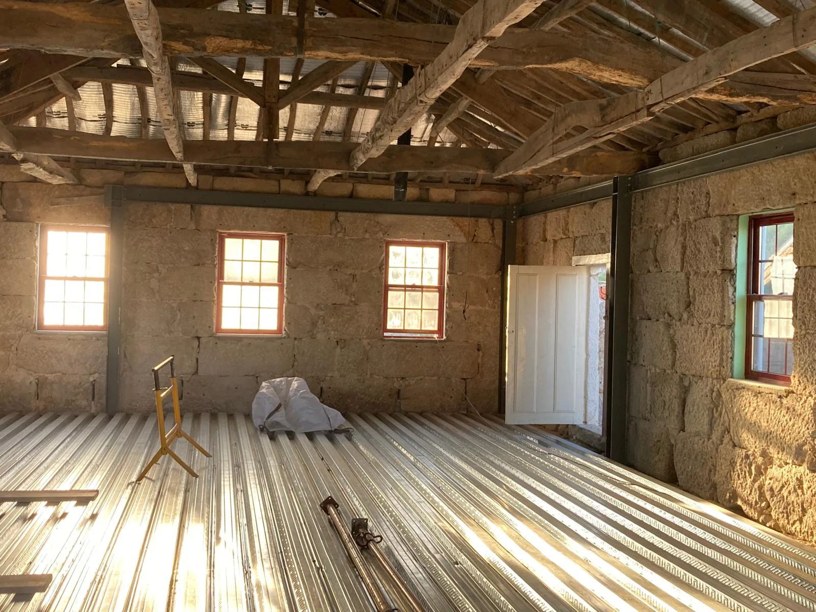 A room with new timber boards laid over the new structure, the granite walls left raw, three small windows and the old roof still open above.