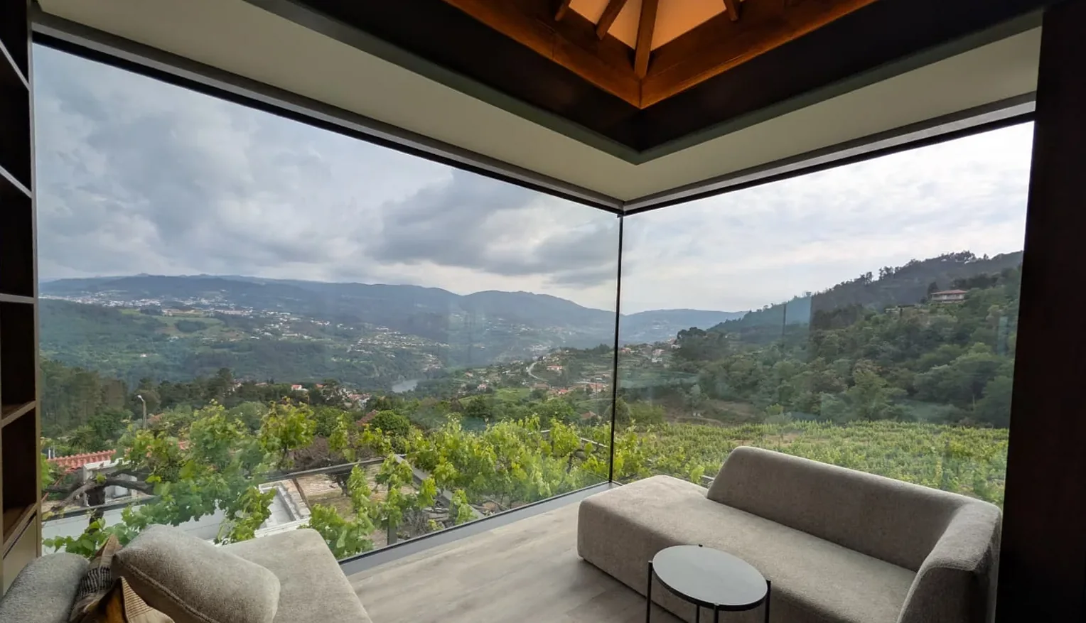 La esquina del salón vista desde dentro: dos planos de vidrio de altura completa que se encuentran sin pilar, abiertos a los bancales de viña y a las colinas al otro lado del valle.