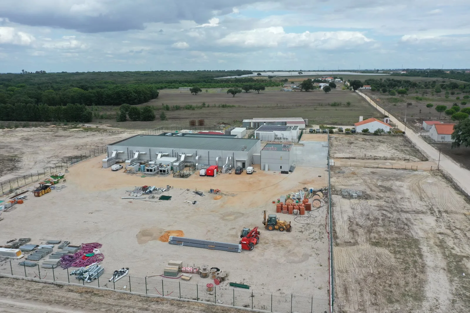 An aerial view of the finished campus: white buildings, a fenced and surfaced yard with plant and equipment, and open country beyond.