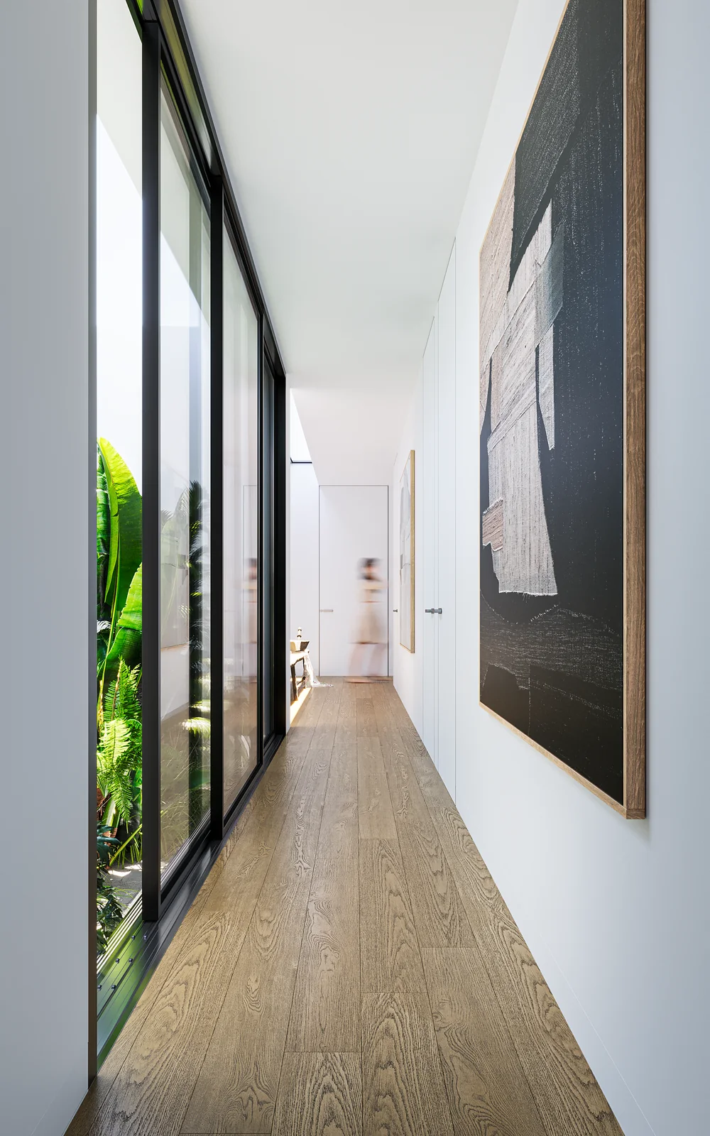 A narrow corridor glazed along one side onto a planted strip, with oak flooring and artwork opposite.