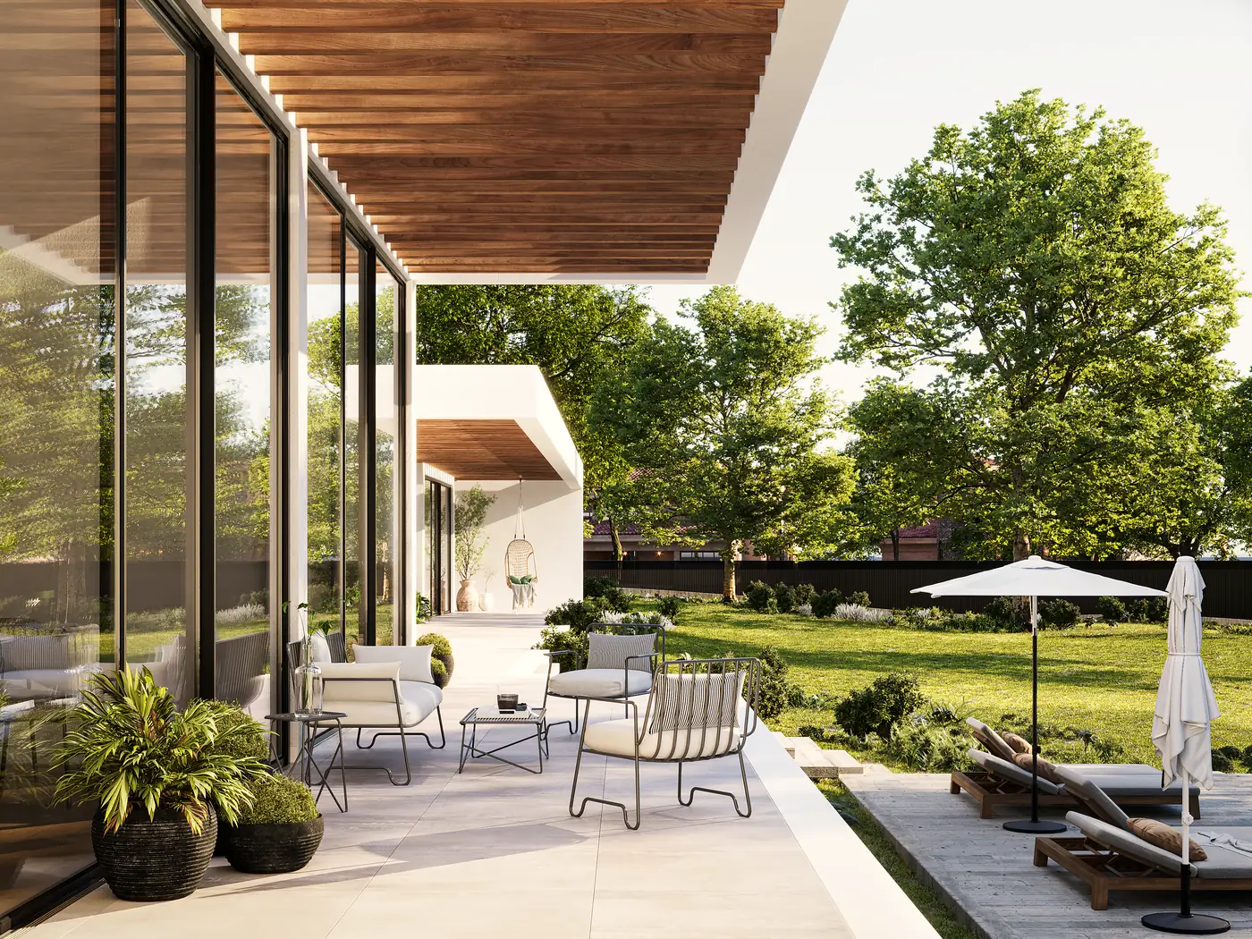 A covered terrace running along a glazed façade, with outdoor seating, a parasol and a lawn beyond.