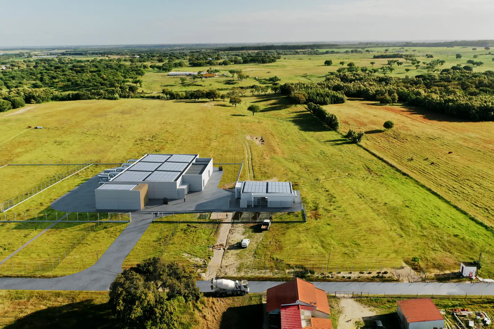 An aerial render of the campus in its landscape: white volumes and a surfaced yard set in green fields and tree lines.
