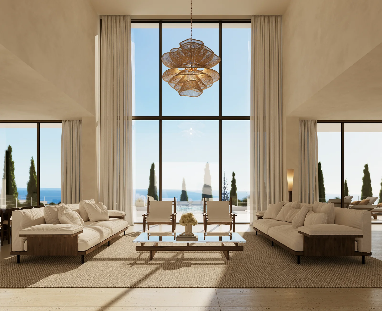 A double-height living room: two low sofas facing each other across a rug, a woven pendant hanging in the void, full-height glazing on three sides and the sea on the horizon.