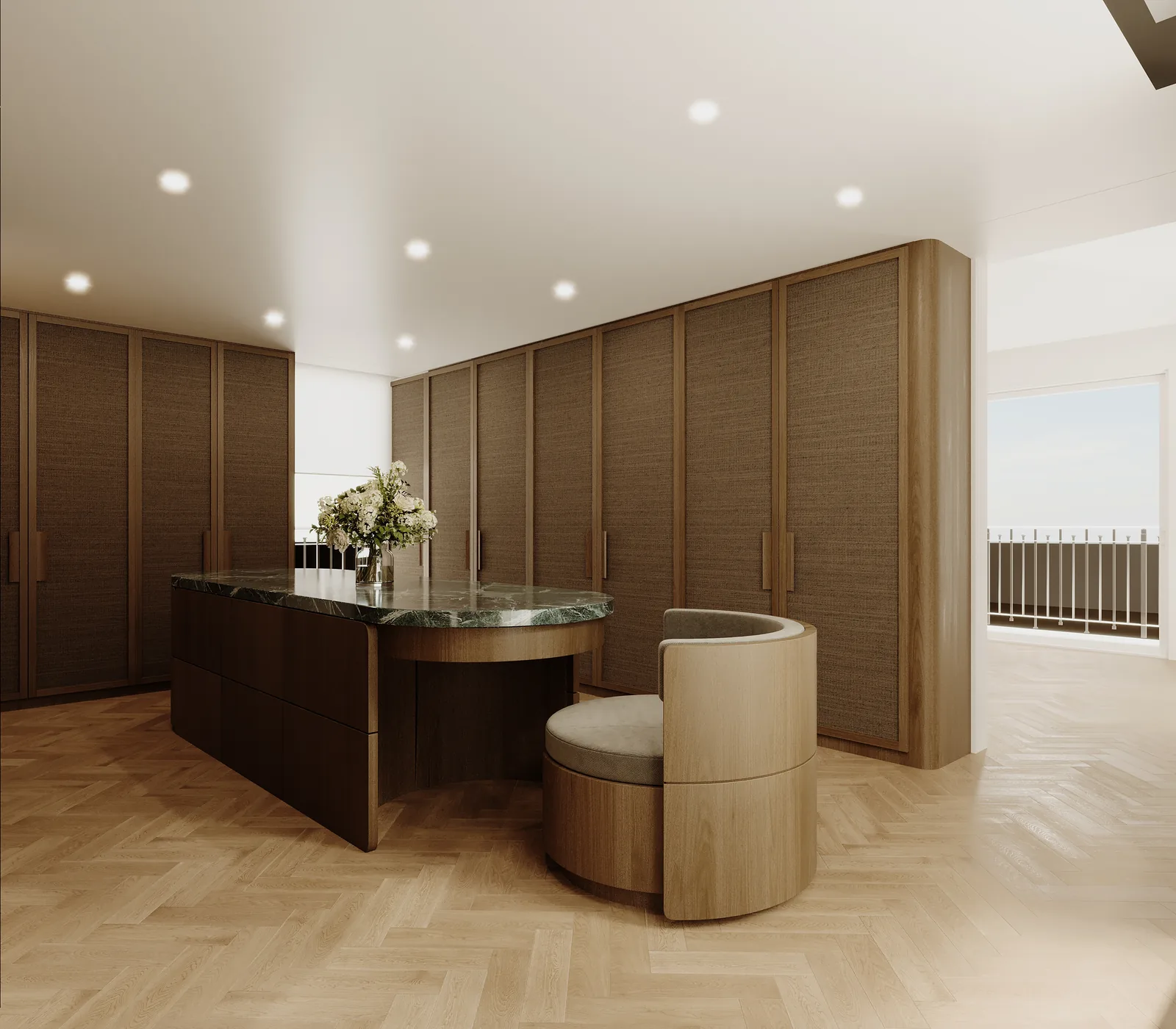 A dressing room lined floor to ceiling in oak with a curved island in the middle carrying a stone top, herringbone parquet underfoot and a window at the far end.