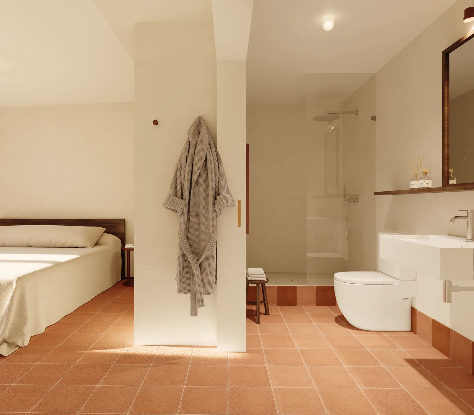 A bathroom open to the bedroom around a freestanding plastered pier: walk-in shower, wall-hung basin and a bathrobe on a hook, all over the same terracotta floor.