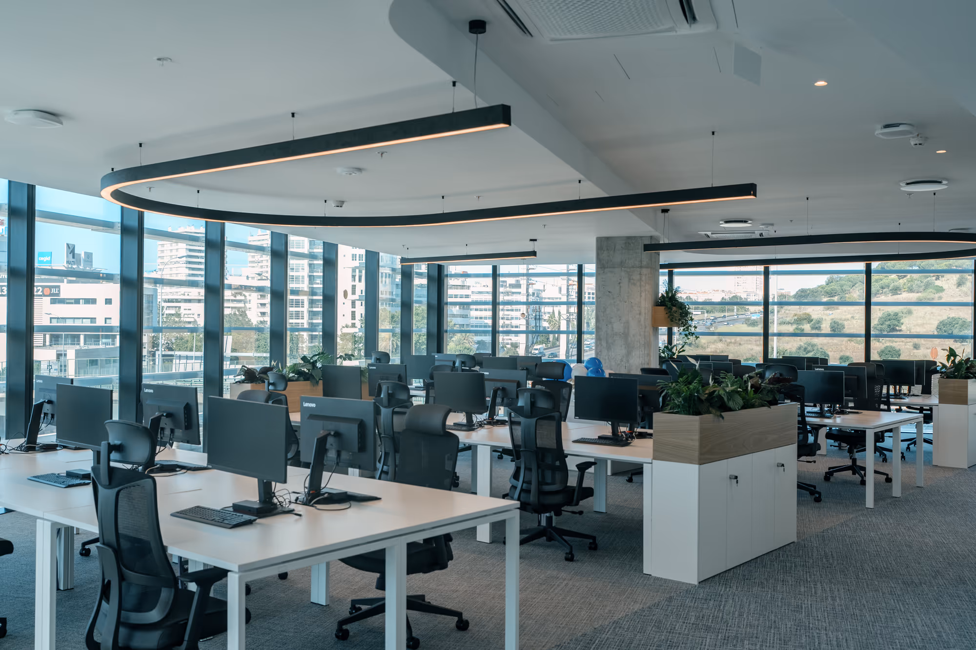 Bright open-plan corporate office with ergonomic workstations and floor-to-ceiling glazing overlooking Lisbon, fitted out by WALLNUT.